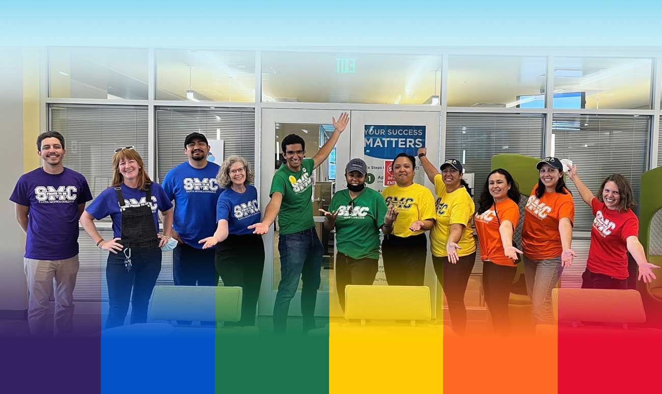 A group of people wearing colorful shirts to form a rainbow